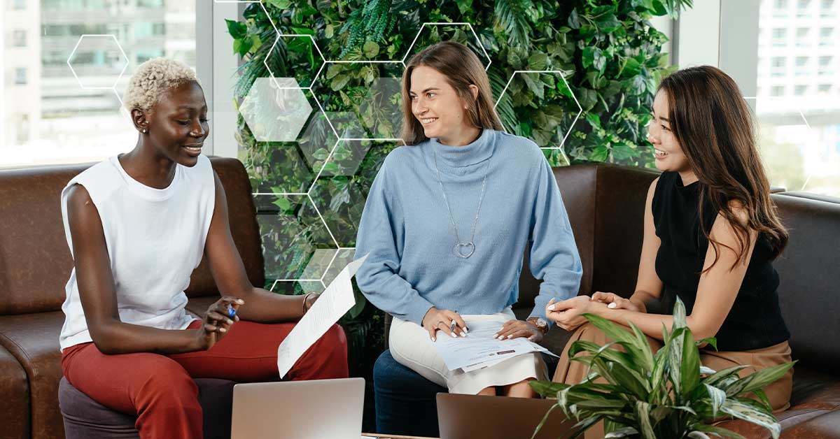 Three women sitting on a couch smiling while going over a document